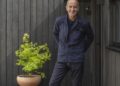 Kevin McCloud stands outside a dark timber home in Grand Designs UK season 24.
