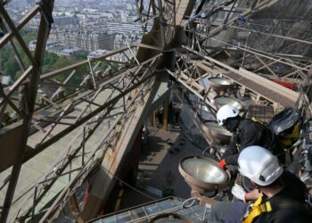 Workers on the Eiffel Tower appear high above Paris in Eiffel Tower: Life Behind The Scenes.