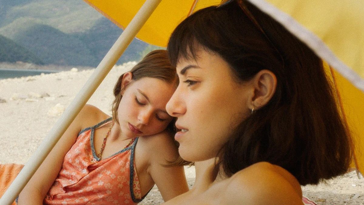 Two women sit beside water in Friends and Strangers on MUBI.