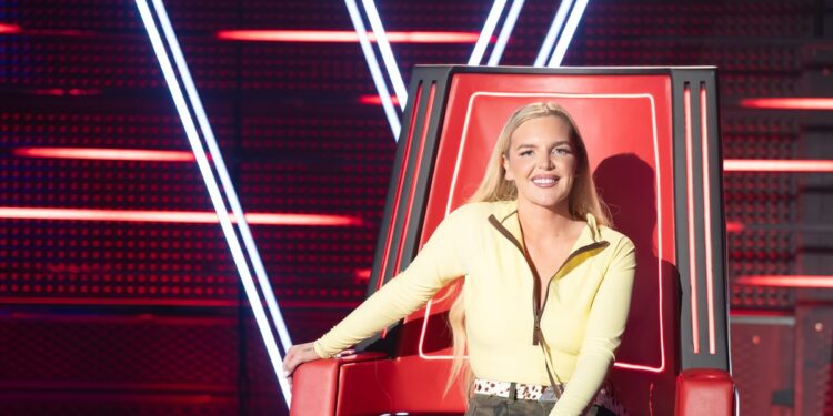 Tones And I seated in a red coach chair on The Voice