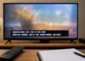 A television screen showing generic caption bars with a remote and broadcast log notebook on a table.