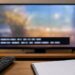 A television screen showing generic caption bars with a remote and broadcast log notebook on a table.