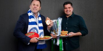 David King and Leigh Montagna pose with breakfast dishes and the premiership cup ahead of the 2026 North Melbourne Grand Final Breakfast.