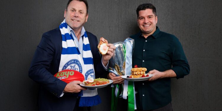 David King and Leigh Montagna pose with breakfast dishes and the premiership cup ahead of the 2026 North Melbourne Grand Final Breakfast.