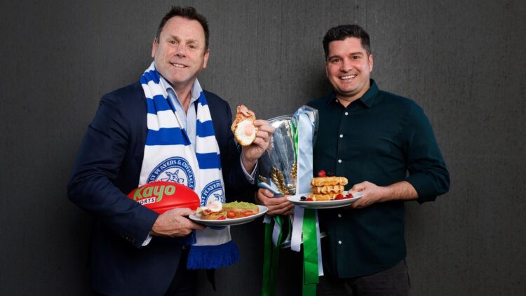 David King and Leigh Montagna pose with breakfast dishes and the premiership cup ahead of the 2026 North Melbourne Grand Final Breakfast.