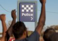 Community members raise their hands near a Northern Territory police sign in 2.6 Seconds: Death in the Outback