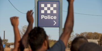 Community members raise their hands near a Northern Territory police sign in 2.6 Seconds: Death in the Outback
