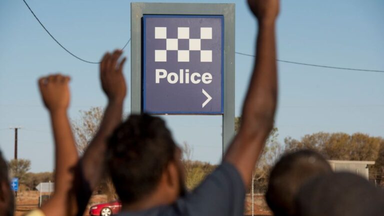 Community members raise their hands near a Northern Territory police sign in 2.6 Seconds: Death in the Outback
