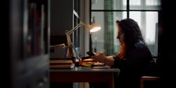 A woman works at a desk by lamplight in Believe in Magic: The Mother of All Cons on ABC