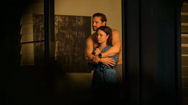 Two characters embrace in a dimly lit room in Dustfall on ABC