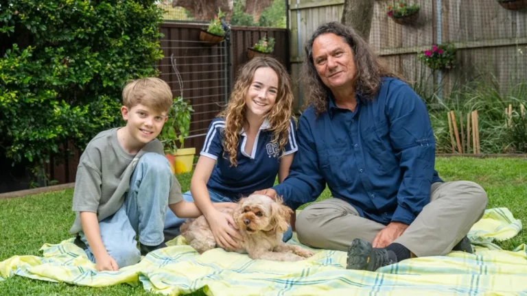 Two children and a presenter on a picnic rug with a dog in Gardening Australia Junior on ABC Kids