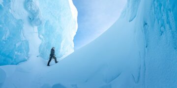 An explorer walks between towering blue ice formations in Ages of Ice
