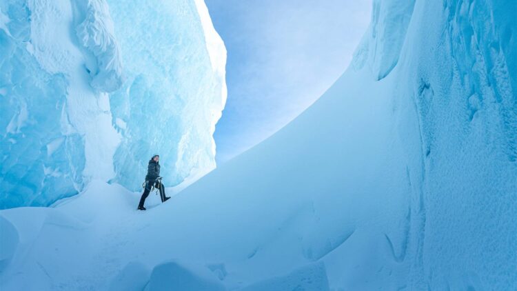 An explorer walks between towering blue ice formations in Ages of Ice