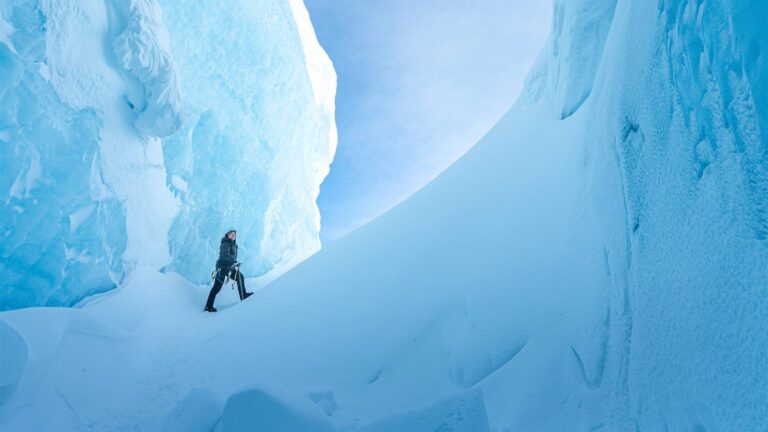 An explorer walks between towering blue ice formations in Ages of Ice