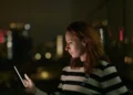A woman looking at a glowing phone in AI Confidential with Hannah Fry