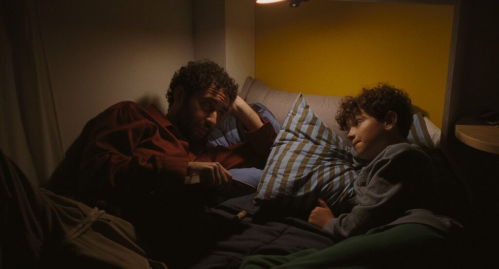 Jordan Firstman and Reggie Absolom lie in bed talking in Club Kid