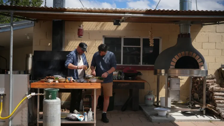 Colin Fassnidge and Manu Feildel prepare food at an outdoor kitchen