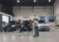 Hannah Fry talks with two people beside cars in a vehicle testing facility