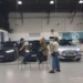 Hannah Fry talks with two people beside cars in a vehicle testing facility